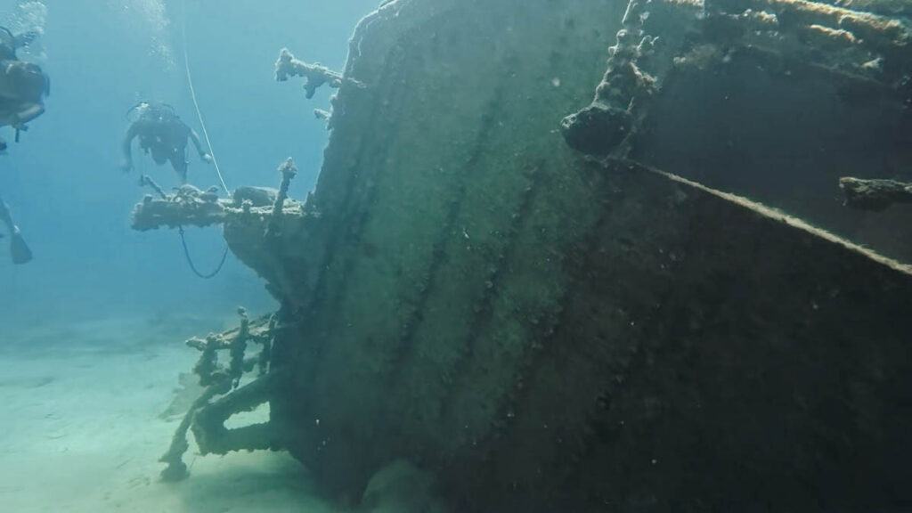 Scuba diver beside a large section of the damaged cargo ship's hull resting on the seabed