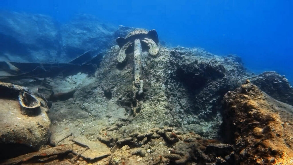 Large ship's anchor resting against rocks and wreckage on the seabed off Cape Apostolos Andreas